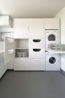 Schrank mit Trockner auf Waschmaschine und zwei Einsätzen mit Platz für jeweils zwei Wäschekörbe.